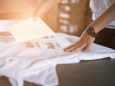 Beyaz tişört üzerine tasarım şablonu yapıştıran adam eli