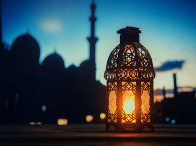 Işık vermekte olan bir fener ile arka planda görünen cami silueti