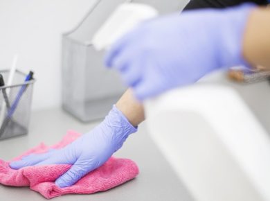 Pembe bir bez ve dezenfektan ile iş yerini temizleyen eldivenli bir kişi
